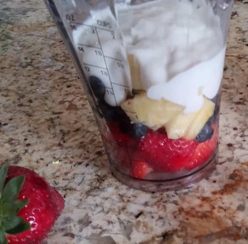 clear blender cup with chopped strawberries, blueberries, pineapple, and cashew yogurt