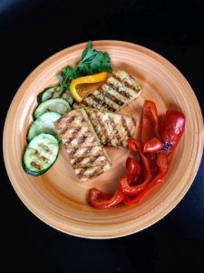3 slices of grilled tofu on orange plat with grilled red peppers and zucchini