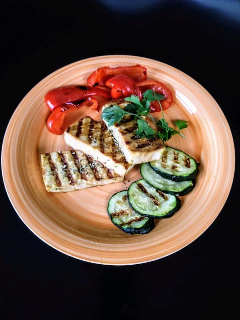 3 slices of grilled tofu on orange plate with cilantro, red peppers, and zucchini