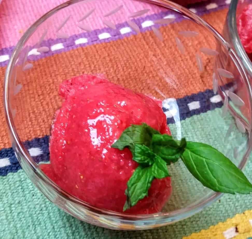 close up scoop of strawberry sorbet with mint leaves in glass bowl
