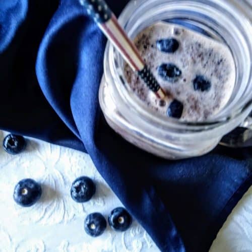 Blueberry smoothie with almond butter in mug with straw on blue napkin