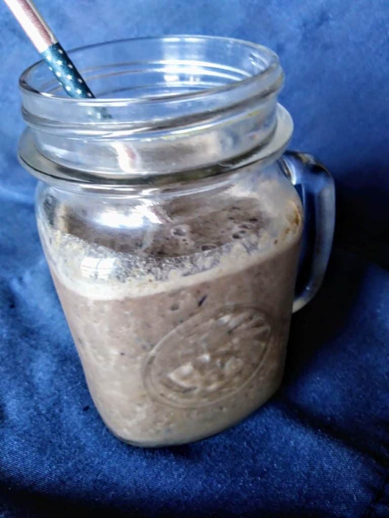Blueberry smoothie with almond butter side view in mug with paper straw