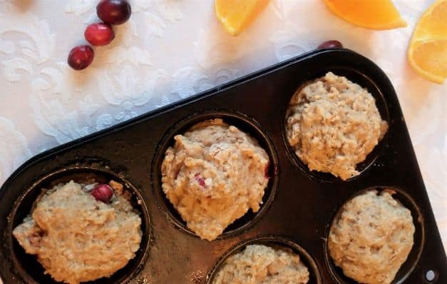 orange cranberry oatmeal muffins in baking tin with cranberries and orange slices nearby