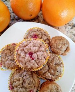 orange cranberry oatmeal muffins on white plate with oranges next to it