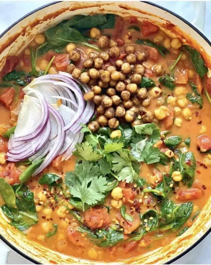 chickpea and spinach curry in bowl with red onion and cilantro leaves
