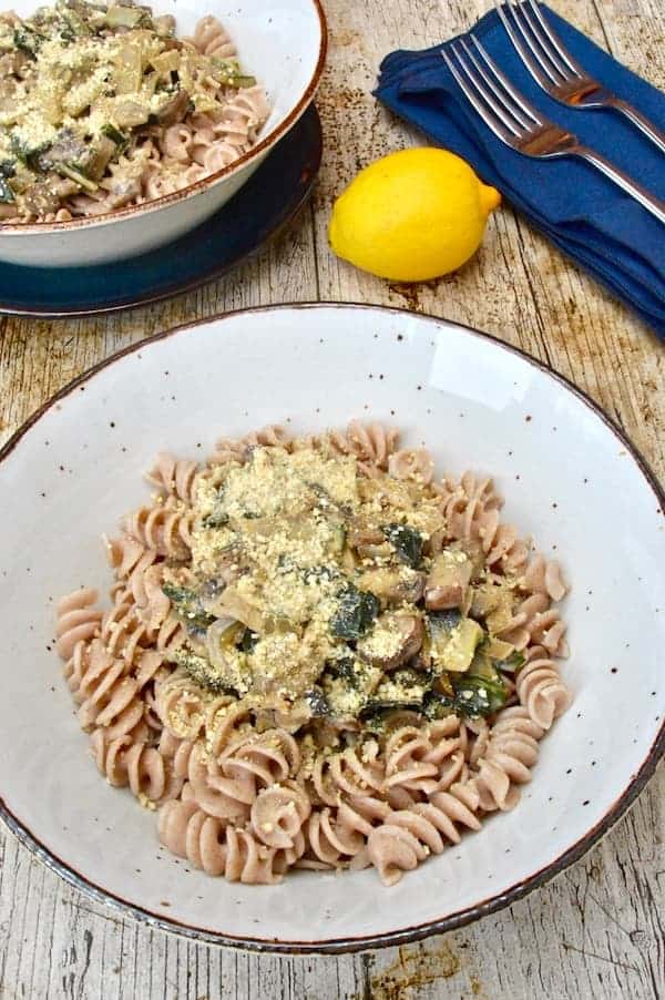 mushrrom and Swiss chard pasta in white bowl with lemon behind it