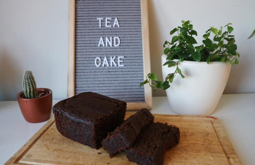 sliced vegan ginger loaf with plant sin background and sign "tea with cake"