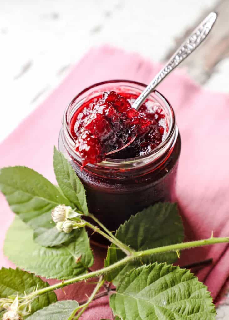 jar of blackberry apple jam with green leaves and spoon