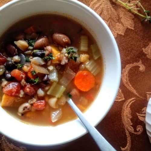 white bowl of 15 bean vegetable soup with spoon and thyme sprig