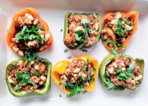 stuffed peppers with butternut squash and quinoa in a white baking dish topped with chopped parsley and basil leaves
