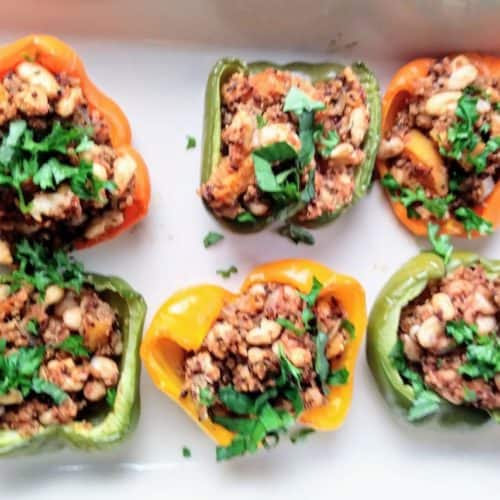 stuffed-peppers-with-butternut-squash-and-quinoa in a white baking dish topped with chopped parsley and basil leaves