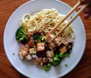 sesame ginger noodles with tofu and vegetables on plate with chopsticks