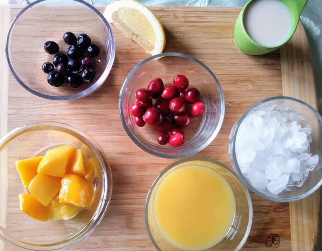 ingredients for cranberry mango smoothie in bowls on cutting board