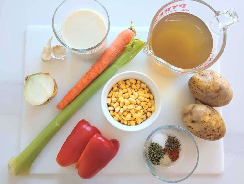 ingredients for easy vegetable corn chowder on cutting board: carrot, celery, potatoes, bell pepper, corn, seasonings.