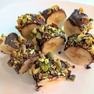 chocolate peanut butter covered banana chunks with pistachios on a plate.
