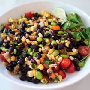 black bean salad with corn and edamame in bowl with lime wedges and fresh cilantro.
