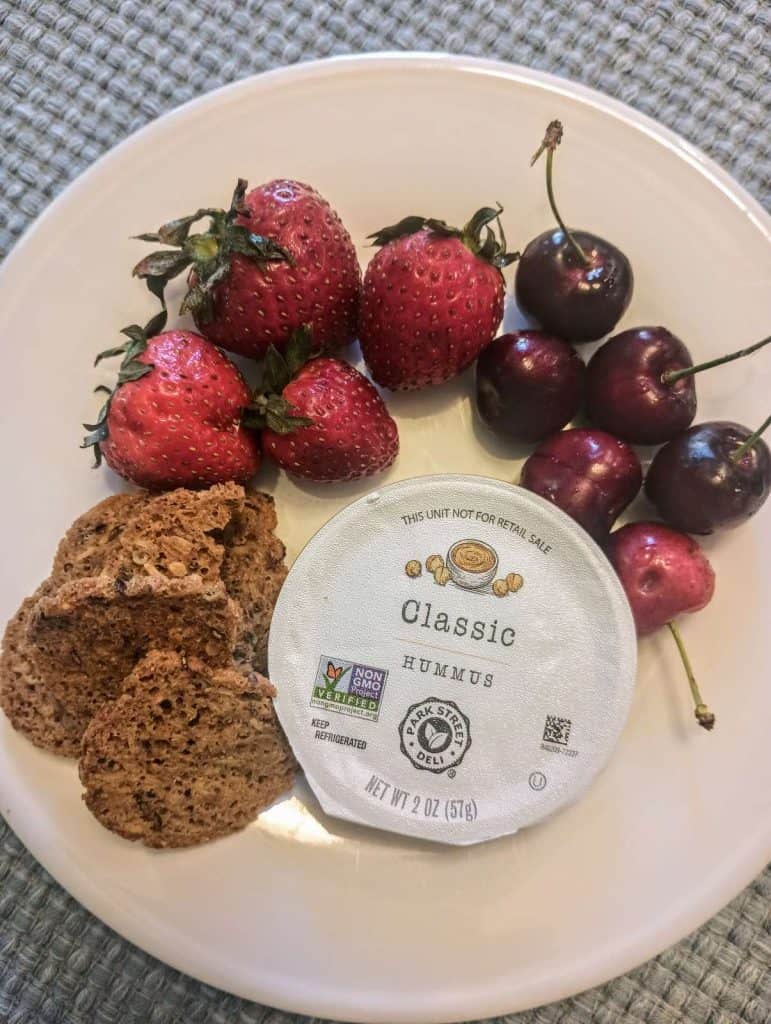 strawberries, cherries, mini sourdough crisps, and small contain of hummus on plate.